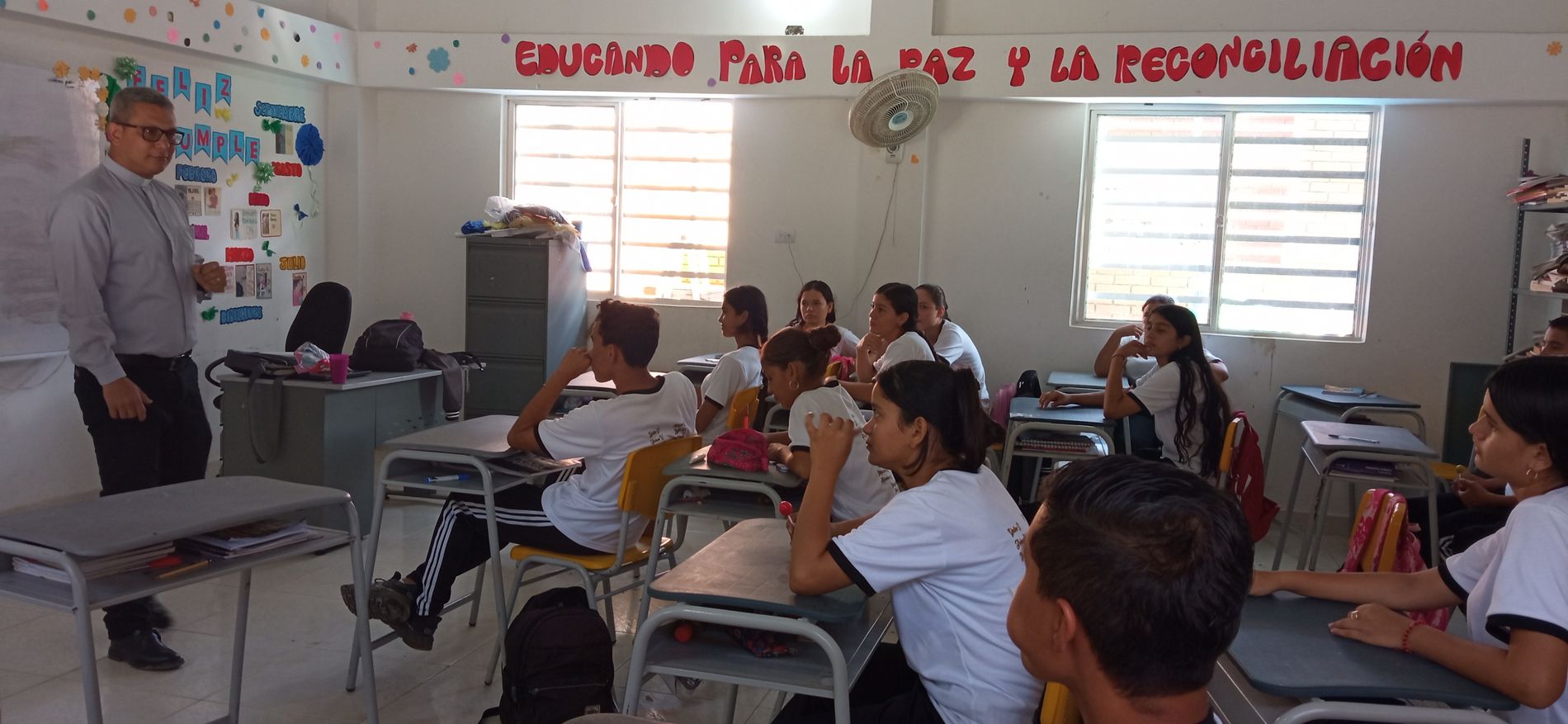 Ein Klassenzimmer mit Jugendlichen. Vorne steht ein ältere Lehrer im grauen Hemd.